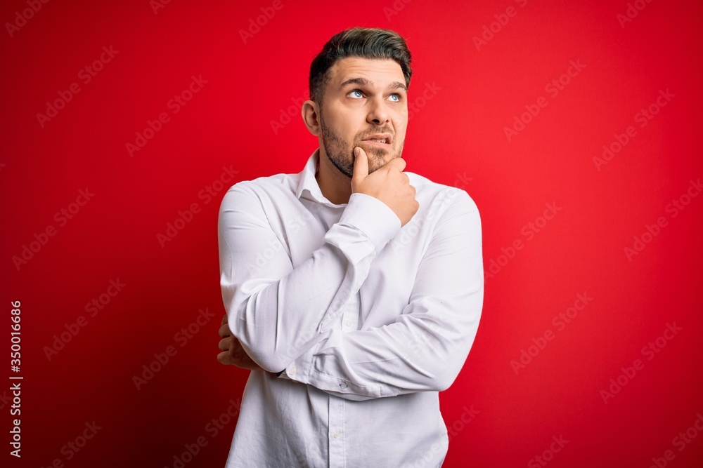 Young business man with blue eyes wearing elegant shirt standing over red isolated background Thinking worried about a question, concerned and nervous with hand on chin Young business man with blue eyes wearing elegant shirt standing over red isolated background Thinking worried about a question, concerned and nervous with hand on chin