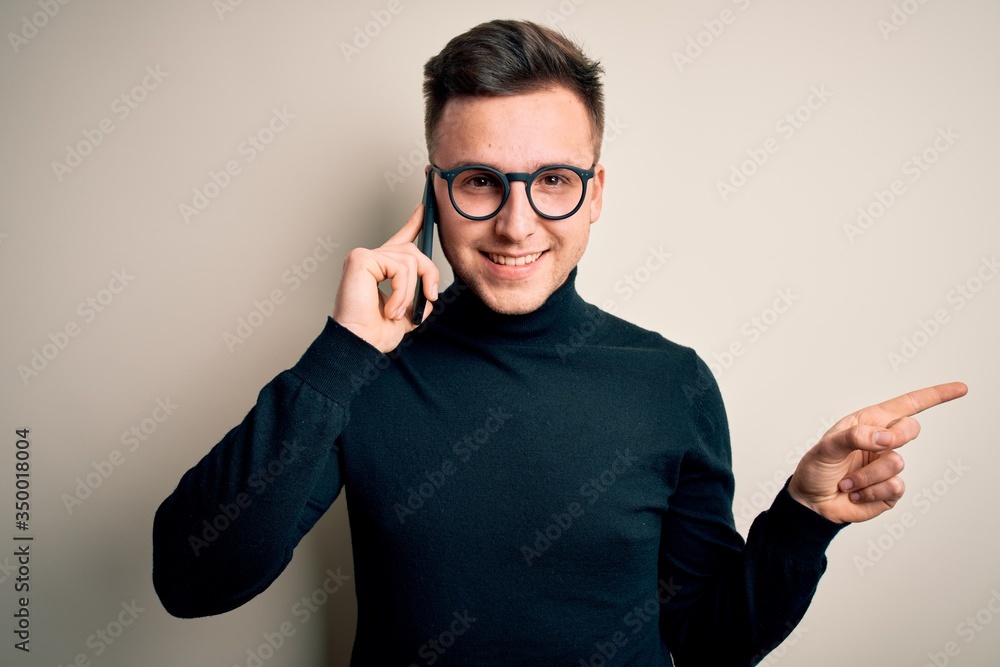 Young handsome caucasian man having a conversation talking on smartphone very happy pointing with hand and finger to the side Young handsome caucasian man having a conversation talking on smartphone very happy pointing with hand and finger to the side