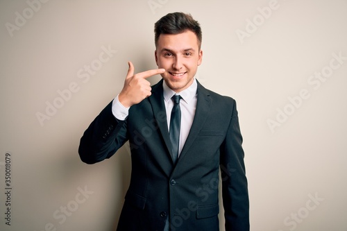 Young handsome business man wearing elegant suit and tie over isolated background Pointing with hand finger to face and nose, smiling cheerful. Beauty concept