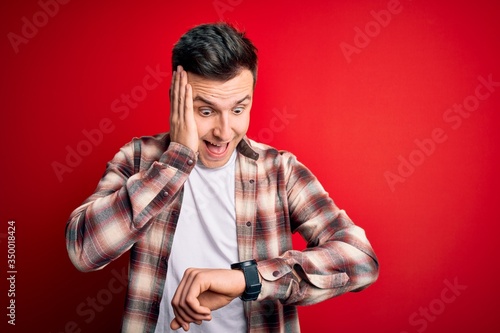 Young handsome caucasian man wearing casual modern shirt over red isolated background Looking at the watch time worried, afraid of getting late