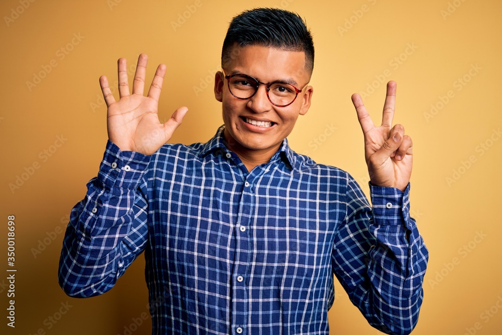 Naklejka premium Young handsome latin man wearing casual shirt and glasses over yellow background showing and pointing up with fingers number seven while smiling confident and happy.