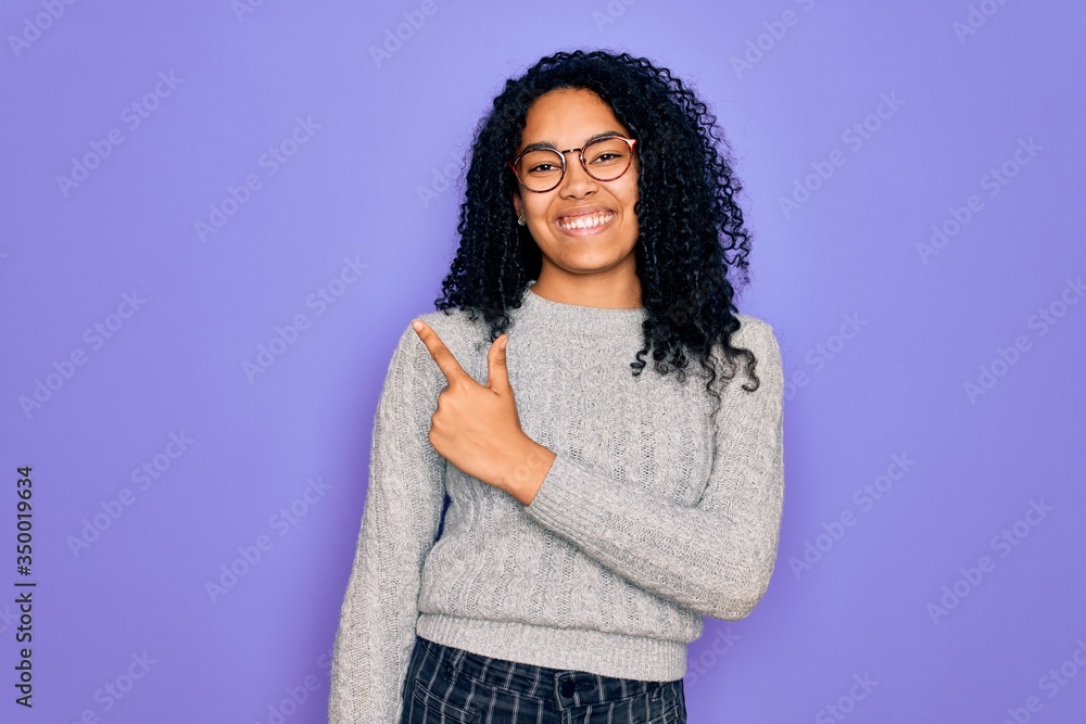 Young african american woman wearing casual sweater and glasses over purple background cheerful with a smile on face pointing with hand and finger up to the side with happy and natural expression Young african american woman wearing casual sweater and glasses over purple background cheerful with a smile on face pointing with hand and finger up to the side with happy and natural expression