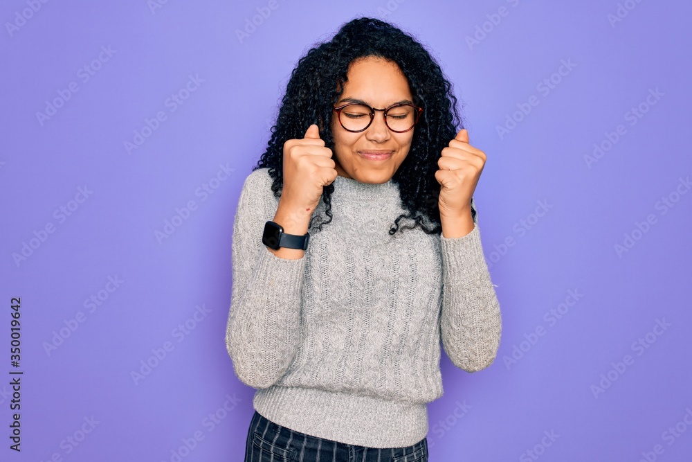 Young african american woman wearing casual sweater and glasses over purple background excited for success with arms raised and eyes closed celebrating victory smiling. Winner concept.