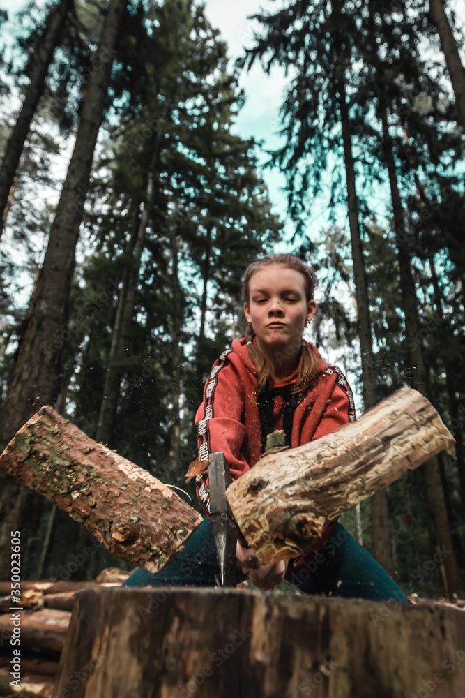Young strong girl teenager chopping wood with axe blow in forest. Purposeful ambitious girl with male character. Hiking, camping and wild travel. Lumberjack woman cuts firewood for bonfire Young strong girl teenager chopping wood with axe blow in forest. Purposeful ambitious girl with male character. Hiking, camping and wild travel. Lumberjack woman cuts firewood for bonfire
