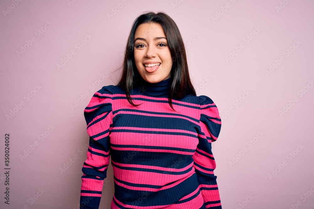 Young brunette elegant woman wearing striped shirt over pink isolated background sticking tongue out happy with funny expression. Emotion concept. Young brunette elegant woman wearing striped shirt over pink isolated background sticking tongue out happy with funny expression. Emotion concept.