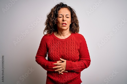 Middle age brunette woman wearing casual sweater standing over isolated white background with hand on stomach because indigestion, painful illness feeling unwell. Ache concept.