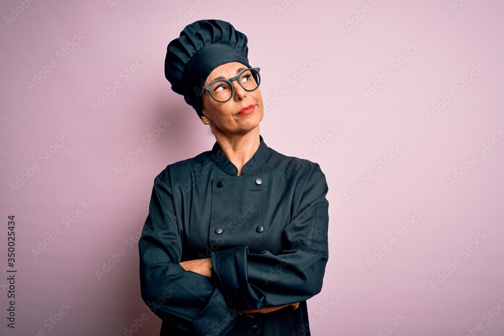 Middle age brunette chef woman wearing cooker uniform and hat over isolated pink background with hand on chin thinking about question, pensive expression. Smiling with thoughtful face. Doubt concept. Middle age brunette chef woman wearing cooker uniform and hat over isolated pink background with hand on chin thinking about question, pensive expression. Smiling with thoughtful face. Doubt concept.