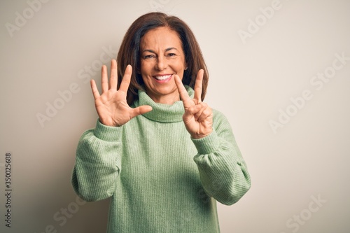 Middle age beautiful woman wearing casual turtleneck sweater over isolated white background showing and pointing up with fingers number seven while smiling confident and happy. photo