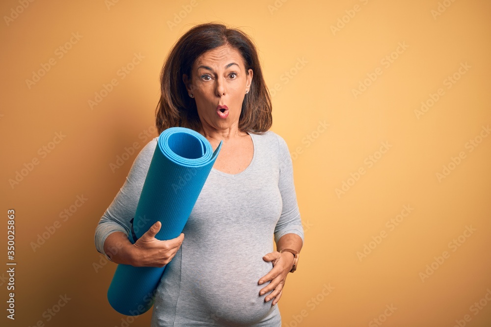 Middle age pregnant woman expecting baby holding yoga mat for healthy lifestyle scared in shock with a surprise face, afraid and excited with fear expression Middle age pregnant woman expecting baby holding yoga mat for healthy lifestyle scared in shock with a surprise face, afraid and excited with fear expression