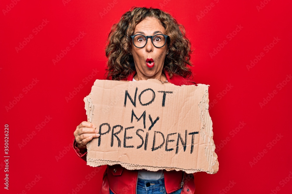 Middle age woman asking for democracy holding banner with not my president message scared and amazed with open mouth for surprise, disbelief face Middle age woman asking for democracy holding banner with not my president message scared and amazed with open mouth for surprise, disbelief face