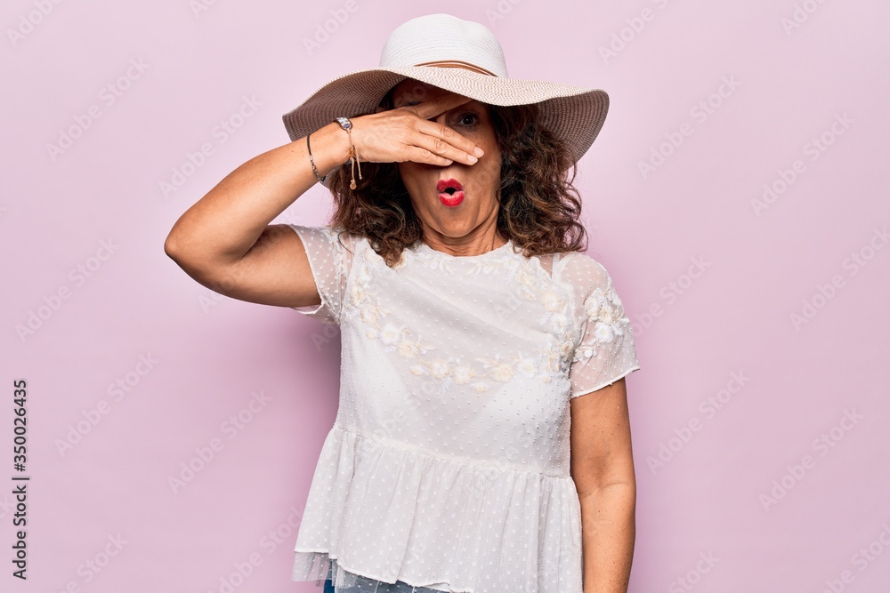 Middle age beautiful woman wearing summer t-shirt and hat over isolated pink background peeking in shock covering face and eyes with hand, looking through fingers afraid Middle age beautiful woman wearing summer t-shirt and hat over isolated pink background peeking in shock covering face and eyes with hand, looking through fingers afraid