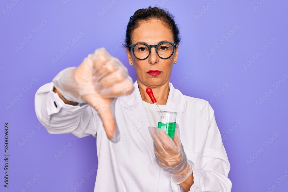 Middle age senior scientist woman wearing laboratory coat holding research test tube with angry face, negative sign showing dislike with thumbs down, rejection concept Middle age senior scientist woman wearing laboratory coat holding research test tube with angry face, negative sign showing dislike with thumbs down, rejection concept