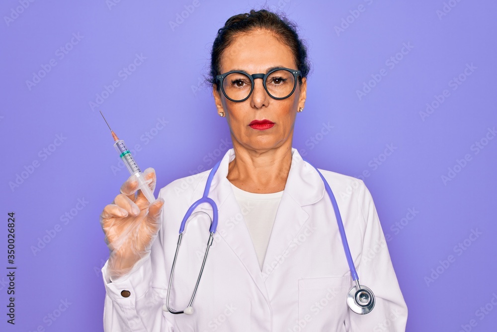 Middle age senior professional doctor woman holding syringe with medical vaccine with a confident expression on smart face thinking serious Middle age senior professional doctor woman holding syringe with medical vaccine with a confident expression on smart face thinking serious