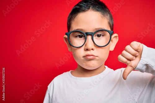 Young little smart boy kid wearing nerd glasses over red isolated background with angry face  negative sign showing dislike with thumbs down  rejection concept