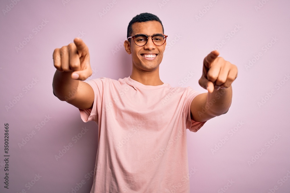 Handsome african american man wearing casual t-shirt and glasses over pink background pointing to you and the camera with fingers, smiling positive and cheerful Handsome african american man wearing casual t-shirt and glasses over pink background pointing to you and the camera with fingers, smiling positive and cheerful