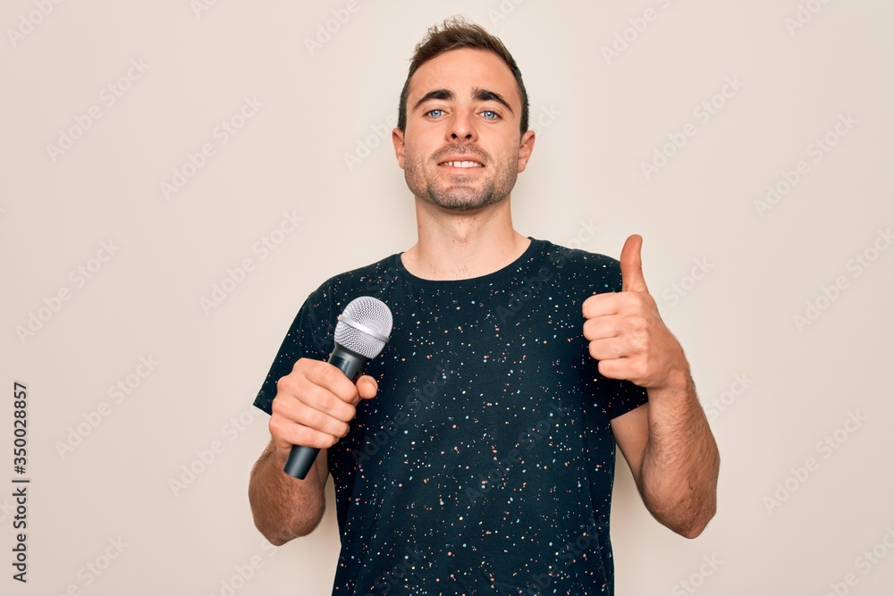 Young handsome singer man with blue eyes singing using microphone over white background happy with big smile doing ok sign, thumb up with fingers, excellent sign Young handsome singer man with blue eyes singing using microphone over white background happy with big smile doing ok sign, thumb up with fingers, excellent sign