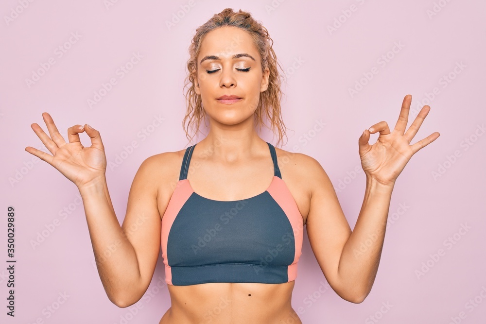 Young beautiful blonde sporty woman doing sport wearing sportswear over pink background relax and smiling with eyes closed doing meditation gesture with fingers. Yoga concept.