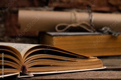 Old books with a scroll and key on a rustic wooden surface on a brick wall background.