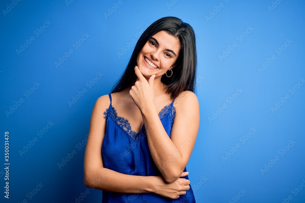 Young beautiful brunette woman wearing elegant and comfortable blue lingerie underwear looking confident at the camera smiling with crossed arms and hand raised on chin. Thinking positive. Young beautiful brunette woman wearing elegant and comfortable blue lingerie underwear looking confident at the camera smiling with crossed arms and hand raised on chin. Thinking positive.