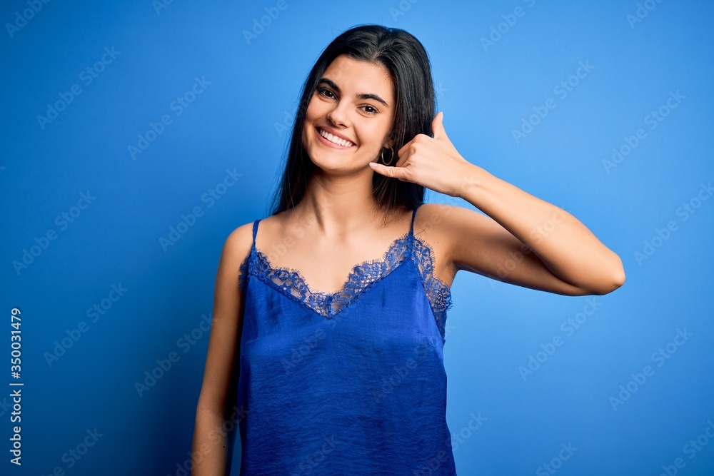 Young beautiful brunette woman wearing elegant and comfortable blue lingerie underwear smiling doing phone gesture with hand and fingers like talking on the telephone. Communicating concepts.