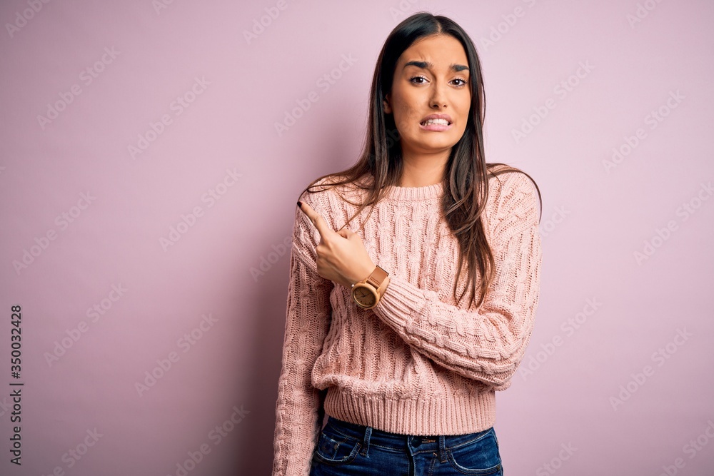 Fototapeta premium Young beautiful brunette woman wearing casual sweater over isolated pink background Pointing aside worried and nervous with forefinger, concerned and surprised expression