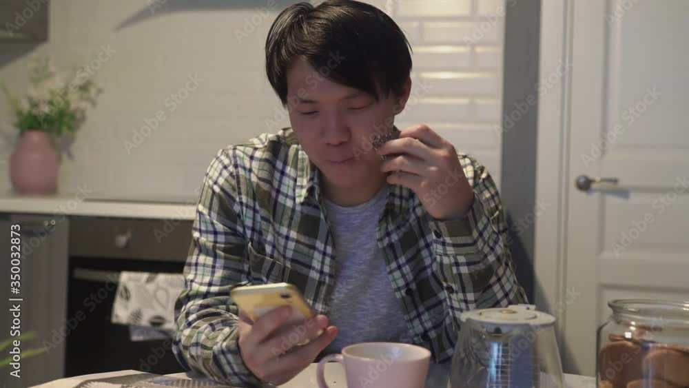 Happy asian man reading something funny on smartphone and smiling in kitchen at home Happy asian man reading something funny on smartphone and smiling in kitchen at home