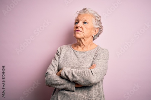 Senior beautiful woman wearing casual t-shirt standing over isolated pink background looking to the side with arms crossed convinced and confident
