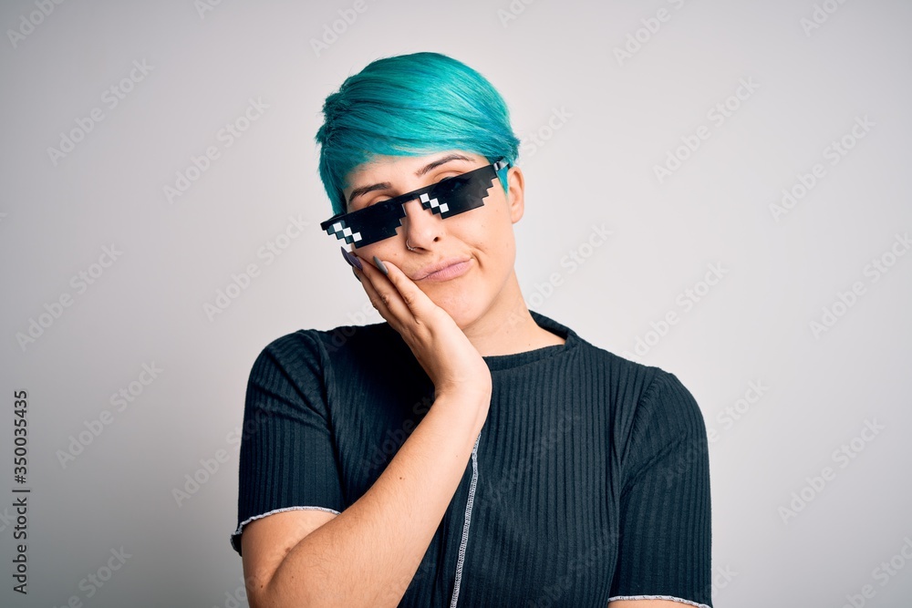 Young woman with blue fashion hair wearing thug life sunglasses over white background thinking looking tired and bored with depression problems with crossed arms. Young woman with blue fashion hair wearing thug life sunglasses over white background thinking looking tired and bored with depression problems with crossed arms.