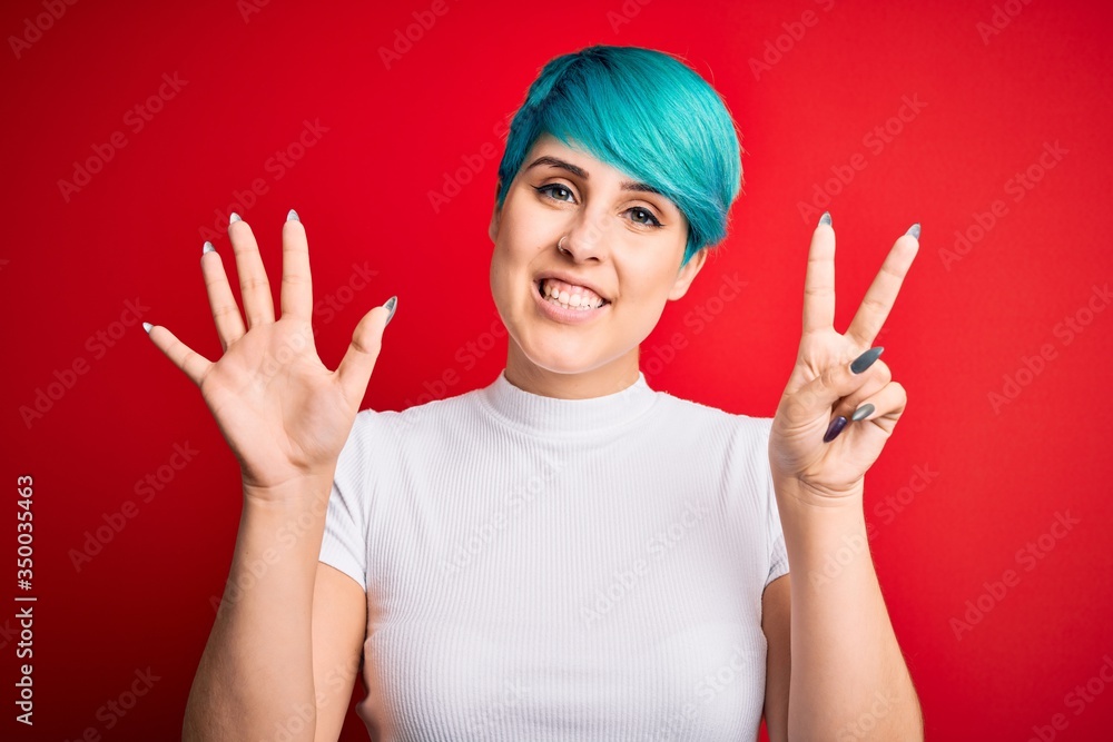 Young beautiful woman with blue fashion hair wearing casual t-shirt over red background showing and pointing up with fingers number seven while smiling confident and happy.