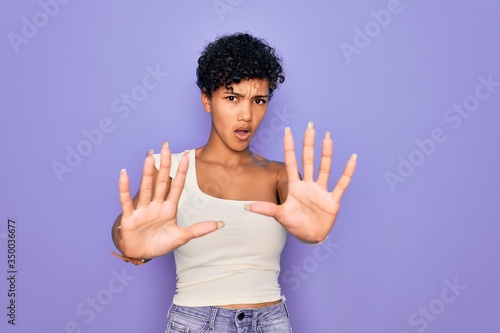 Young beautiful african american afro woman wearing casual t-shirt over purple background doing stop gesture with hands palms, angry and frustration expression