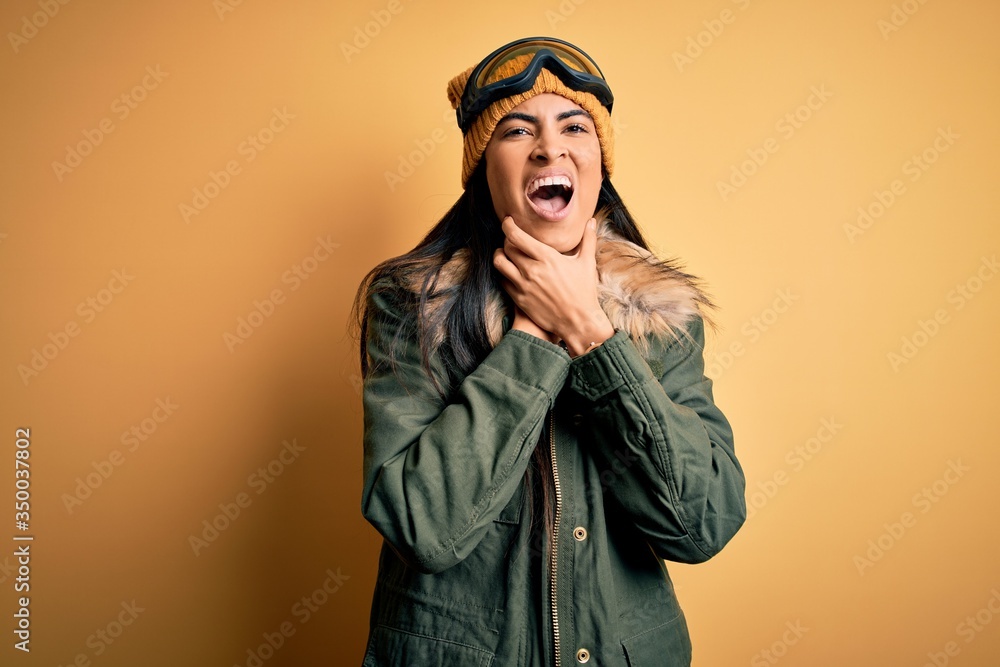 Young beautiful hispanic woman wearing ski glasses and coat for winter weather shouting suffocate because painful strangle. Health problem. Asphyxiate and suicide concept. Young beautiful hispanic woman wearing ski glasses and coat for winter weather shouting suffocate because painful strangle. Health problem. Asphyxiate and suicide concept.