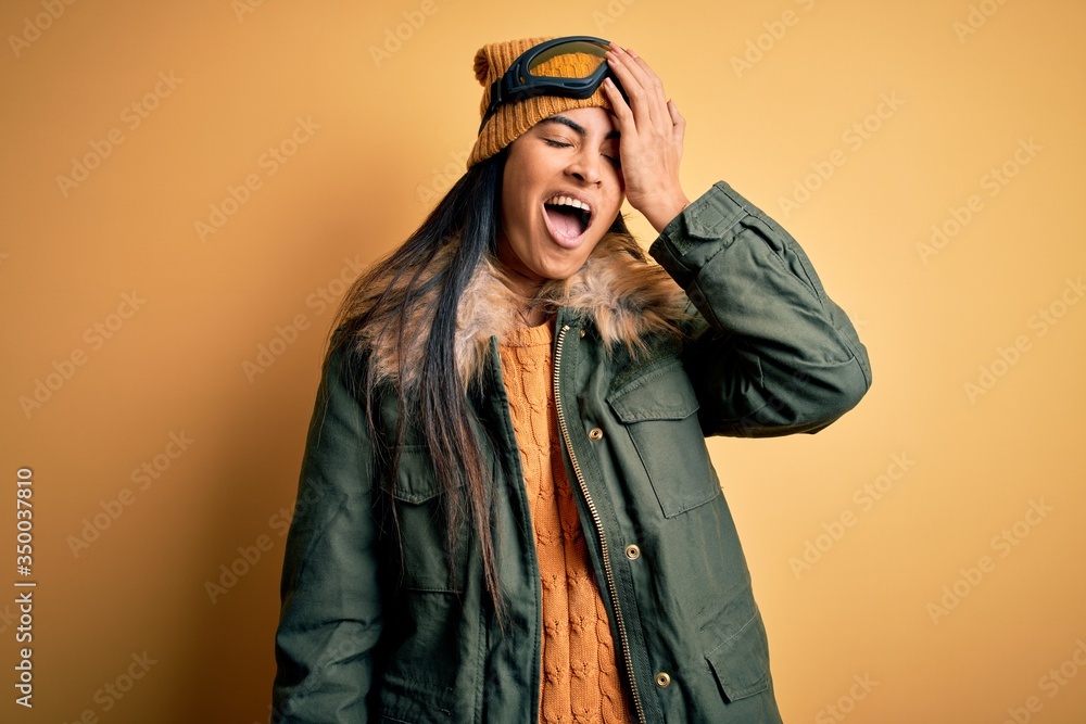 Young beautiful hispanic woman wearing ski glasses and coat for winter weather Yawning tired covering half face, eye and mouth with hand. Face hurts in pain. Young beautiful hispanic woman wearing ski glasses and coat for winter weather Yawning tired covering half face, eye and mouth with hand. Face hurts in pain.