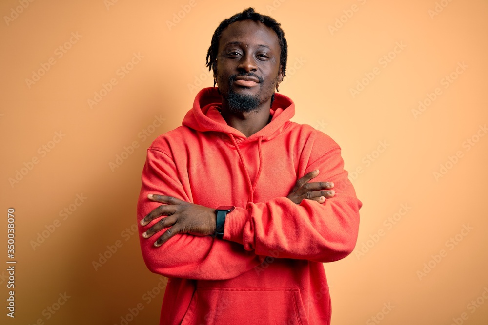 Young african american sporty man wearing sweatshirt with hoodie over yellow background happy face smiling with crossed arms looking at the camera. Positive person. Young african american sporty man wearing sweatshirt with hoodie over yellow background happy face smiling with crossed arms looking at the camera. Positive person.