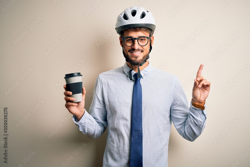 Young businessman wearing glasses and bike helmet drinking cup of coffee surprised with an idea or question pointing finger with happy face, number one Young businessman wearing glasses and bike helmet drinking cup of coffee surprised with an idea or question pointing finger with happy face, number one
