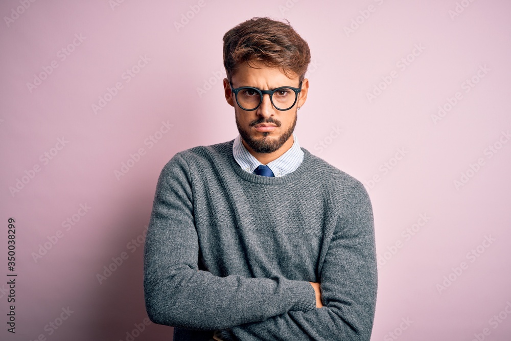 Young handsome man with beard wearing glasses and sweater standing over pink background skeptic and nervous, disapproving expression on face with crossed arms. Negative person. Young handsome man with beard wearing glasses and sweater standing over pink background skeptic and nervous, disapproving expression on face with crossed arms. Negative person.