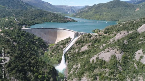 AERIAL DRONE SMOOTH FORWARD APPROACH TO IMMENSE OPENED DAM GATE OF RESERVOIR IN STUNNING PYRENEES GREEN VALLEY