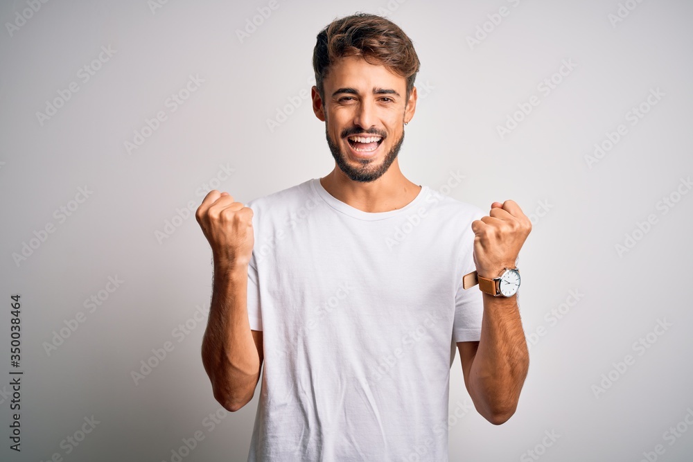 Fototapeta premium Young handsome man with beard wearing casual t-shirt standing over white background celebrating surprised and amazed for success with arms raised and open eyes. Winner concept.