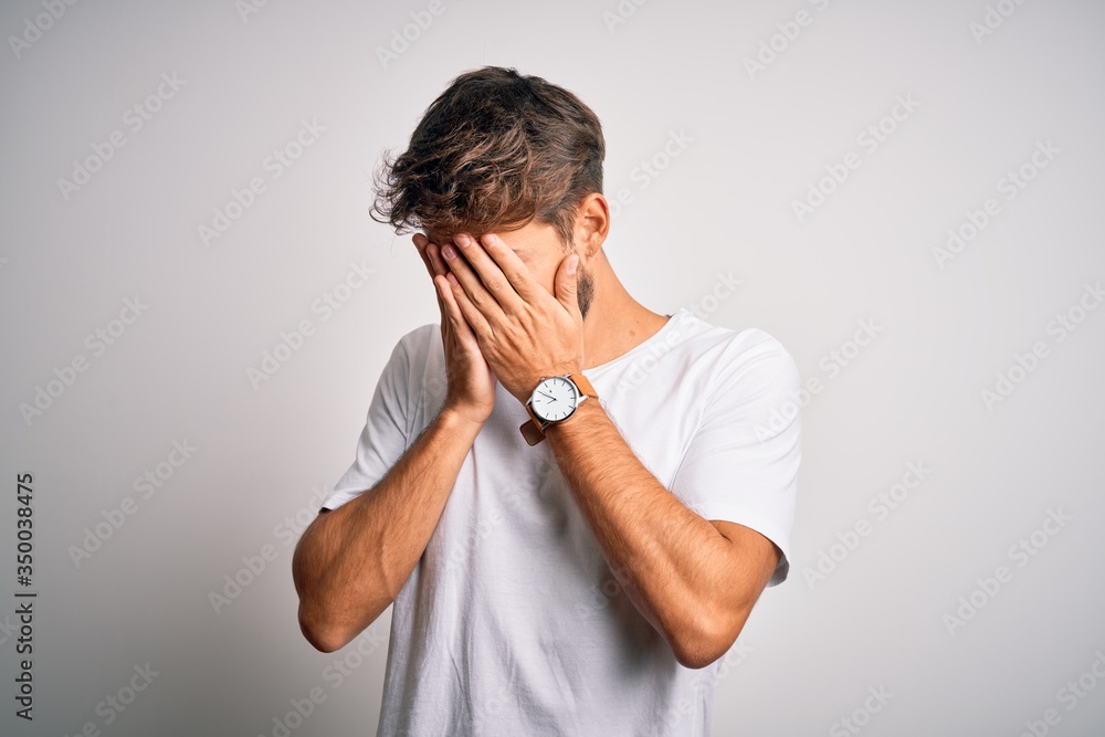 Young handsome man with beard wearing casual t-shirt standing over white background with sad expression covering face with hands while crying. Depression concept. Young handsome man with beard wearing casual t-shirt standing over white background with sad expression covering face with hands while crying. Depression concept.