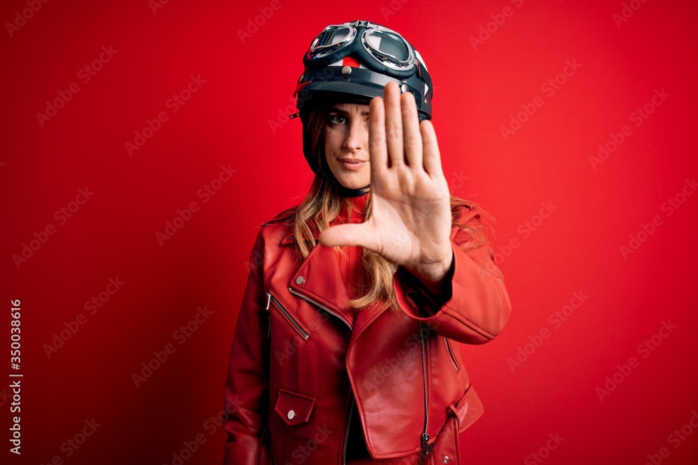 Φωτογραφία Young beautiful brunette motrocyclist woman wearing moto helmet over red background doing stop sing with palm of the hand