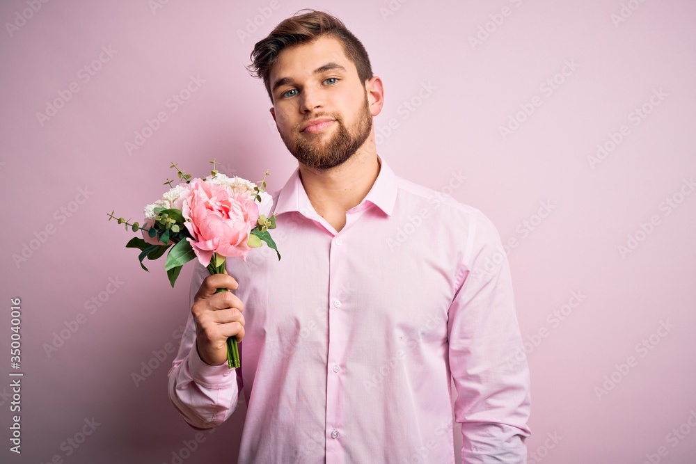 Young blond romantic man with beard and blue eyes holding beautiful bouquet of flowers with a confident expression on smart face thinking serious Young blond romantic man with beard and blue eyes holding beautiful bouquet of flowers with a confident expression on smart face thinking serious