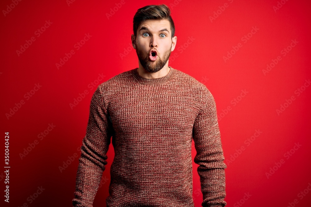 Young blond man with beard and blue eyes wearing casual sweater over red background afraid and shocked with surprise expression, fear and excited face. Young blond man with beard and blue eyes wearing casual sweater over red background afraid and shocked with surprise expression, fear and excited face.