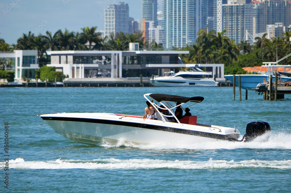 Obraz premium White motor boat with black trim powered by a single outboard engine cruising on Biscayne Bay off Miami Beach,Florida