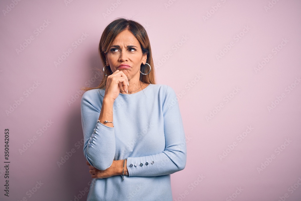 Middle age beautiful woman wearing casual t-shirt standing over isolated pink background with hand on chin thinking about question, pensive expression. Smiling with thoughtful face. Doubt concept. Middle age beautiful woman wearing casual t-shirt standing over isolated pink background with hand on chin thinking about question, pensive expression. Smiling with thoughtful face. Doubt concept.