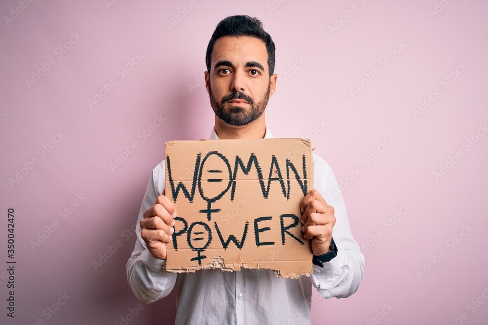 Activist man with beard asking for women rights holding banner with woman power message with a confident expression on smart face thinking serious Activist man with beard asking for women rights holding banner with woman power message with a confident expression on smart face thinking serious
