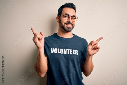 Handsome man with beard wearing t-shirt with volunteer message over white background smiling confident pointing with fingers to different directions. Copy space for advertisement