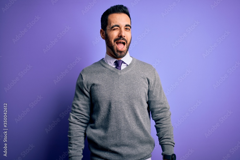 Handsome businessman with beard wearing casual tie standing over purple background winking looking at the camera with sexy expression, cheerful and happy face. Handsome businessman with beard wearing casual tie standing over purple background winking looking at the camera with sexy expression, cheerful and happy face.