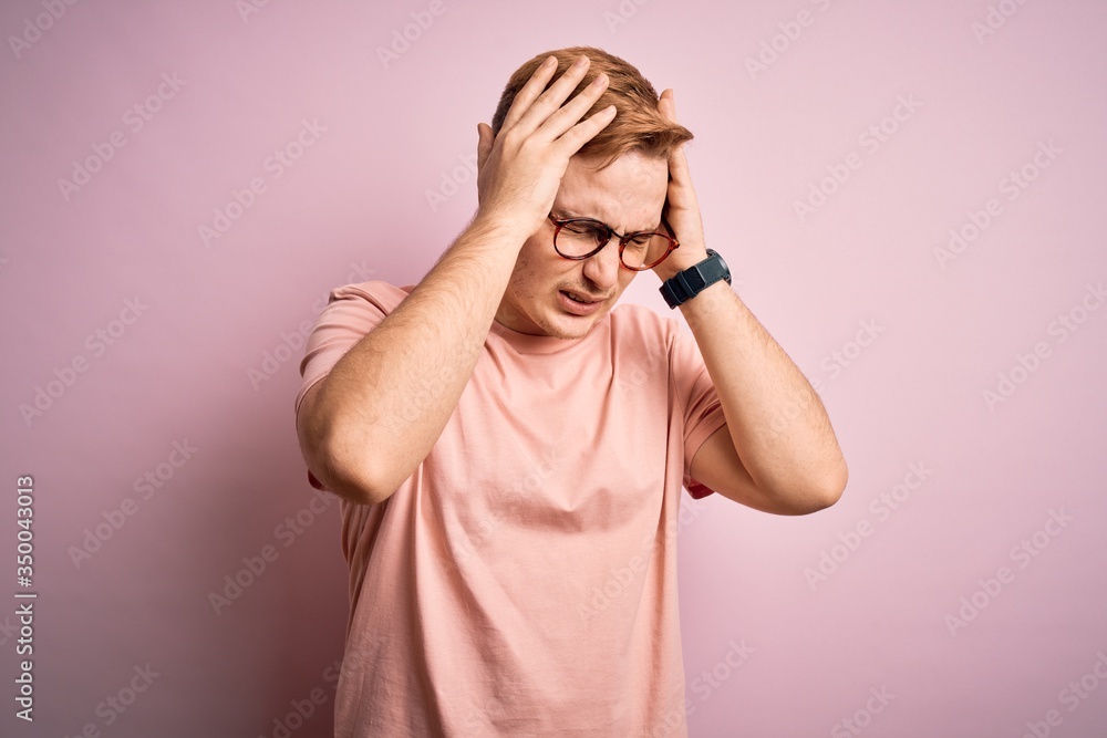 Young handsome redhead man wearing casual t-shirt standing over isolated pink background suffering from headache desperate and stressed because pain and migraine. Hands on head. Young handsome redhead man wearing casual t-shirt standing over isolated pink background suffering from headache desperate and stressed because pain and migraine. Hands on head.