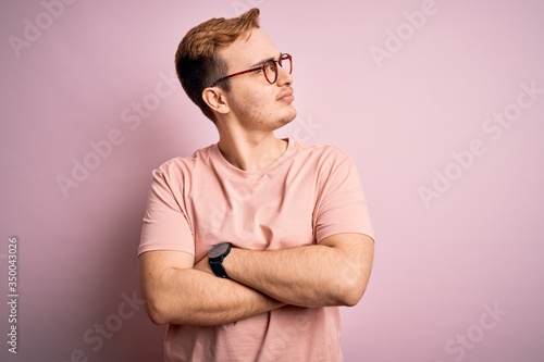 Young handsome redhead man wearing casual t-shirt standing over isolated pink background looking to the side with arms crossed convinced and confident