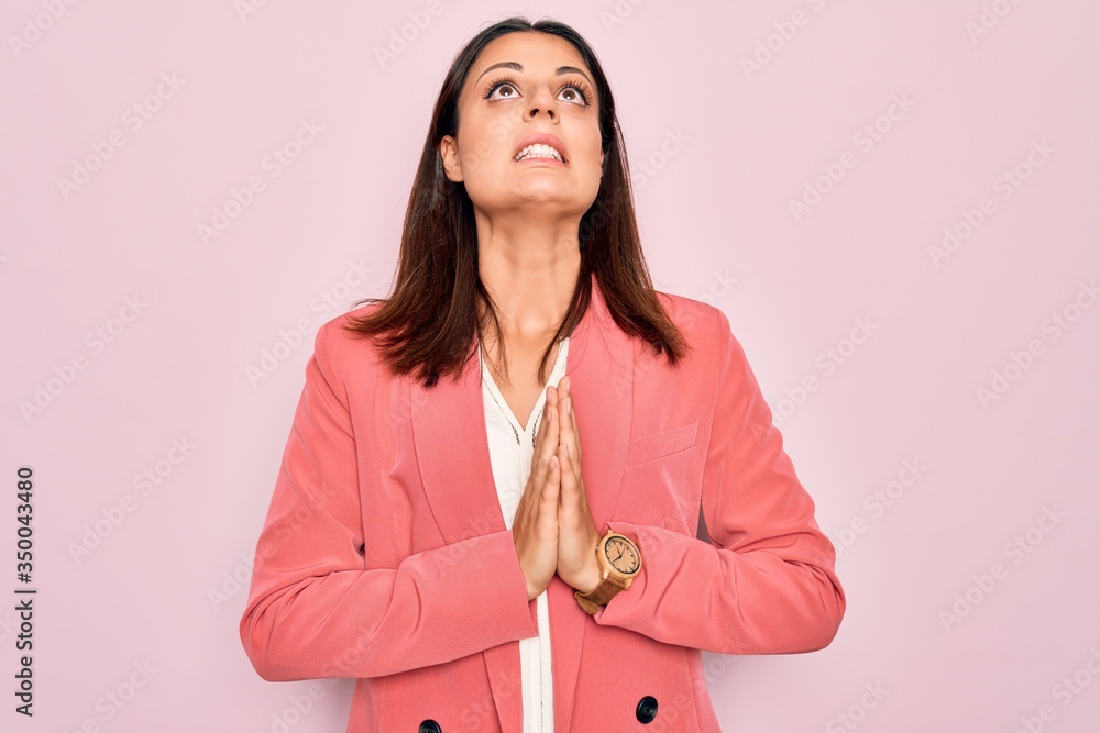 Young beautiful brunette businesswoman wearing elegant jacket over isolated pink background begging and praying with hands together with hope expression on face very emotional and worried. Begging. Young beautiful brunette businesswoman wearing elegant jacket over isolated pink background begging and praying with hands together with hope expression on face very emotional and worried. Begging.