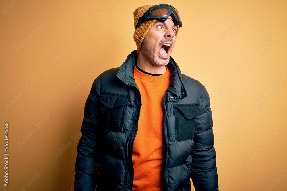 Young handsome skier man skiing wearing snow sportswear using ski goggles angry and mad screaming frustrated and furious, shouting with anger. Rage and aggressive concept. Young handsome skier man skiing wearing snow sportswear using ski goggles angry and mad screaming frustrated and furious, shouting with anger. Rage and aggressive concept.